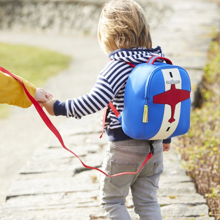 Young child wearing red and blue airplane harness bag with red tether.