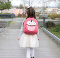 Young girl wearing a pink backpack with a large cupcake applique design. 