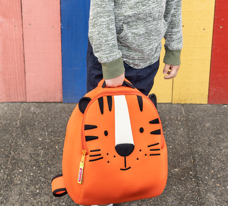 Dabbawalla Bags Tiger backpack featuring smiling face of tiger with black and white applique on orange body.Active young blonde boy climbing play structure with bright orange and black tiger backpack.