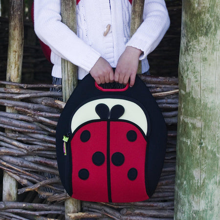 Small girl carrying Dabbawalla Bags Cute as a Ladybug insulated lunch Bag while exploring outside.