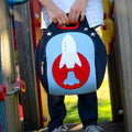 School child holding space theme washable lunch box.  Space rocket design appliqued on front of  lightweight lunch tote.  Dabbawalla Bags are sustainable, re-usable, PVC, PBA Phthalate free.