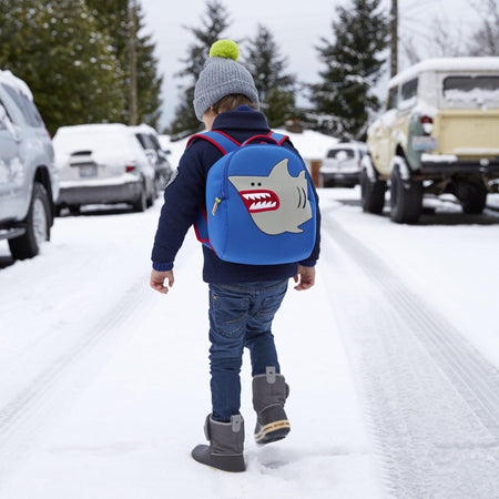 Young boy stomping through snow wearing shark-theme backpack. 